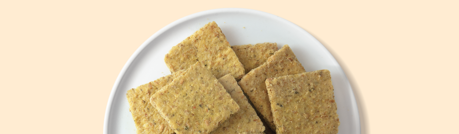 A white plate with rectangular, seed-speckled crackers stacked on it, set against a light beige background.