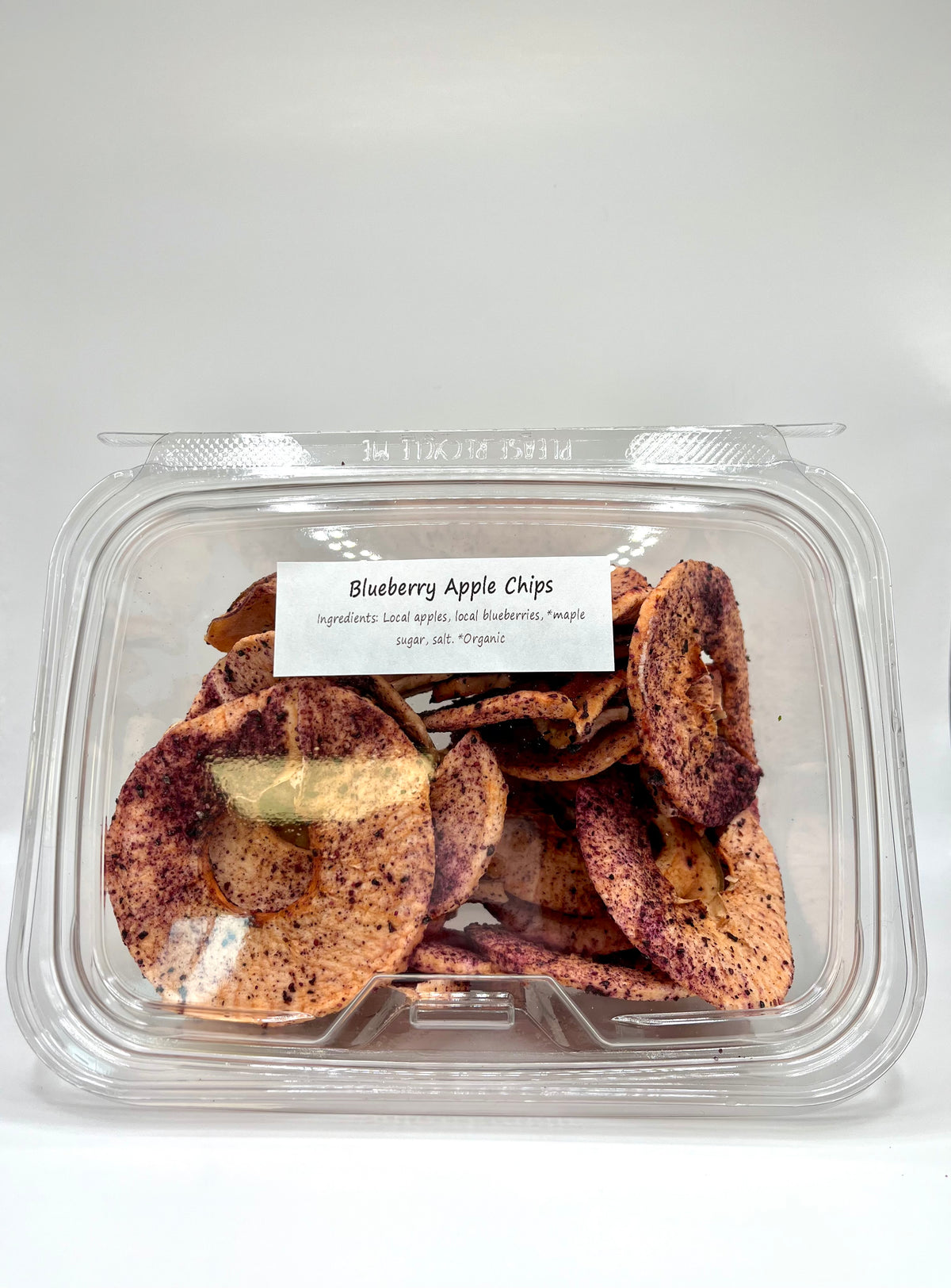A clear plastic container holds Blueberry Apple Chips by Healing Home Foods—round dried apple chips dusted with blueberry powder, made from organic apples, blueberries, maple sugar, and a touch of salt.