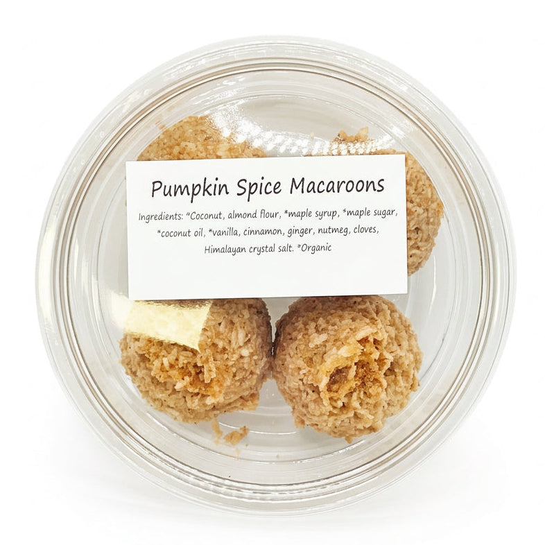 A clear plastic round container holding several pumpkin spice macaroons, with a white label reading 'Pumpkin Spice Macaroons' and ingredient text, photographed against a plain light background.